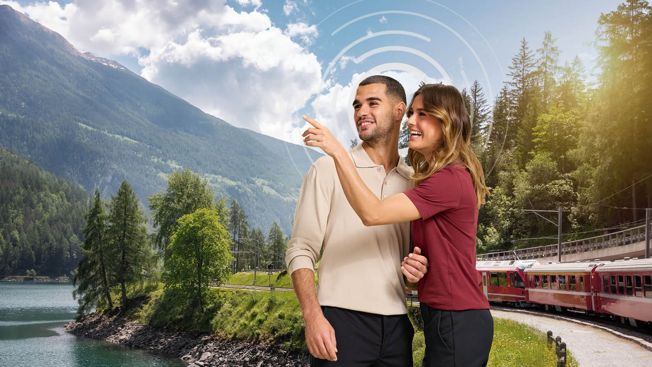 Pareja en un bonito paisaje verde, con el tren pasando detrás de ellos.